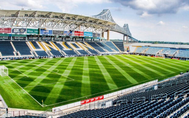 A soccer stadium in Pennsylvania with well maintained green grass and a large bridge in the background