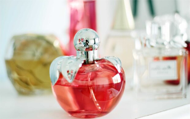 A red perfume bottle shaped like an apple with silver leaves on a white surface