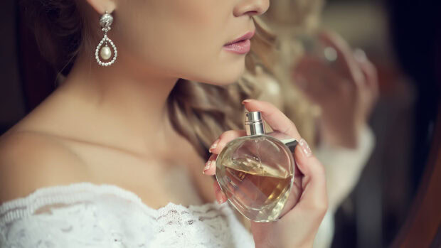 Woman holding perfume bottle in elegant lace dress with pearl earrings