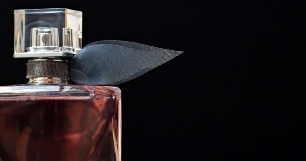 Close up of perfume bottle with black ribbon neck detail on black background