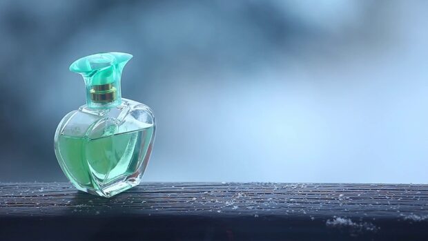 A green perfume bottle with a decorative cap on a wooden surface with snowflakes visible