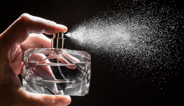 A hand holding a perfume spray bottle releasing mist into the air