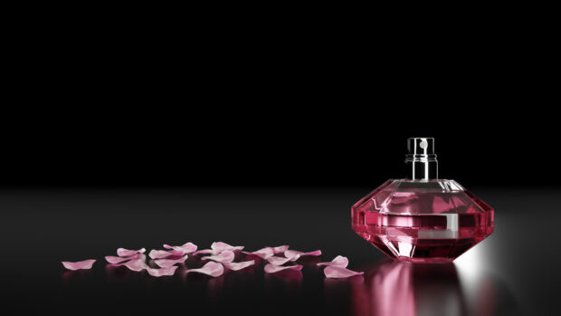 A pink perfume bottle with scattered rose petals on a reflective black surface