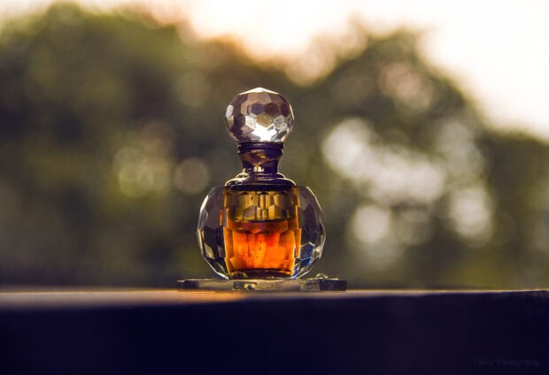 A vintage bottle of perfume with golden liquid inside placed on a surface during sunset