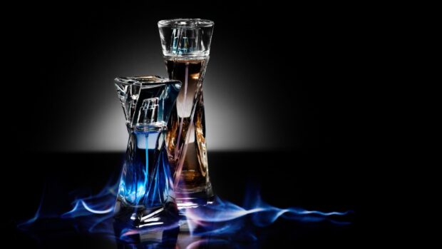 Two perfume bottles with blue and brown liquid on black background with smoke effects