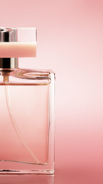A clear perfume bottle with pink liquid on a soft pink background