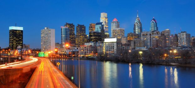 Philadelphia city skyline at dusk with lit buildings and highway light trails reflecting on river