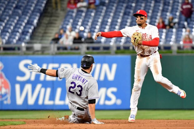 A Philadelphia Phillies player throws the baseball during an infield play against a sliding opponent