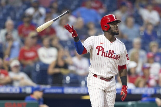 A Philadelphia Phillies player in a white pinstripe uniform tossing a bat during a baseball game