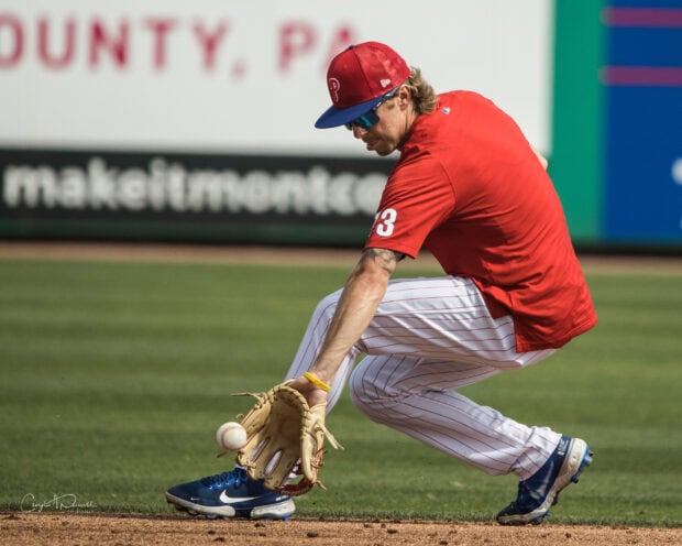 Philadelphia Phillies player wearing red uniform fielding a baseball on the grass in a game