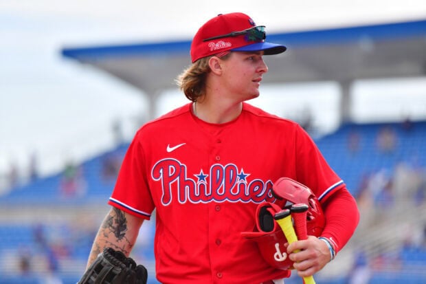 A Philadelphia Phillies player in red jersey holding a helmet and baseball bats on the field