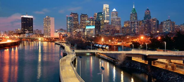 Philly skyline with illuminated buildings and a riverfront walkway at dusk