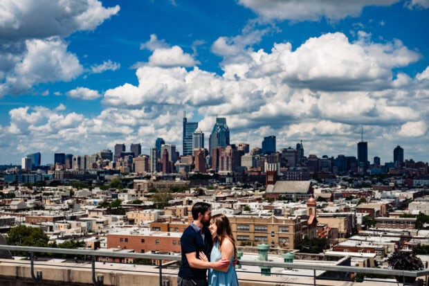 A couple embracing with Philly skyline in the background under a partly cloudy sky