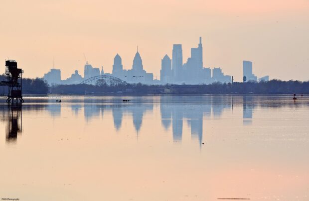 Philly Skyline Wallpaper 2K Desktop A distant view of the Philly skyline reflected on calm water during sunrise with soft orange sky