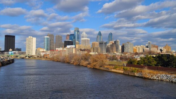 Philly skyline with river and city buildings under a partly cloudy sky