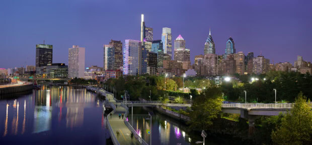 Evening view of Philly skyline along the river with illuminated buildings and walking paths