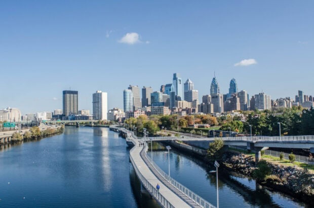 A clear view of Philly skyline along the river with a pedestrian walkway and blue sky