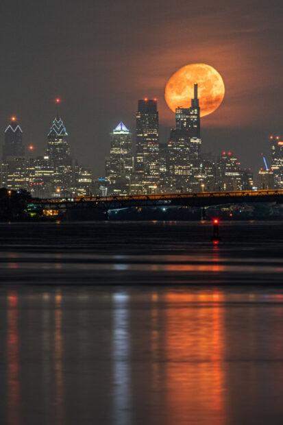 The Philly skyline with a large orange moon glowing behind the buildings at night