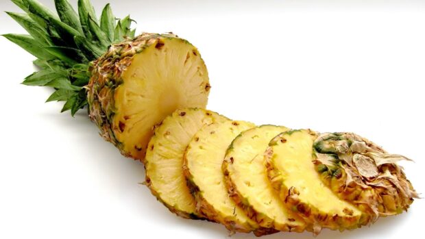Fresh pineapple sliced with green leaves on a white surface