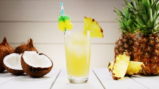 A refreshing pineapple drink with a slice of pineapple and coconuts on a white wooden surface