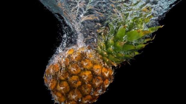 A ripe pineapple submerged in water with bubbles surrounding it against a black background
