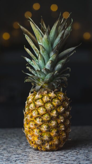 A ripe pineapple standing on a granite surface with blurred lights in the background