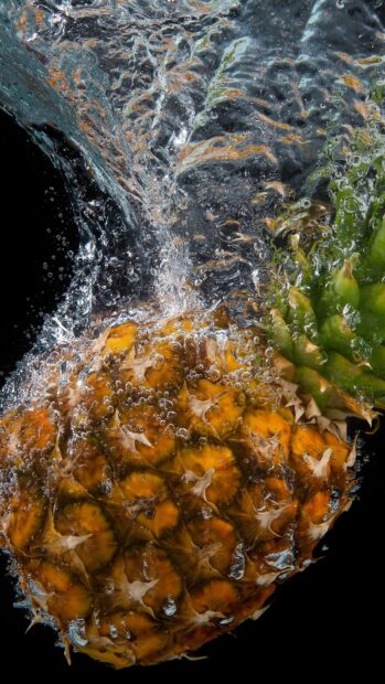Fresh pineapple submerged in water with bubbles on a black background
