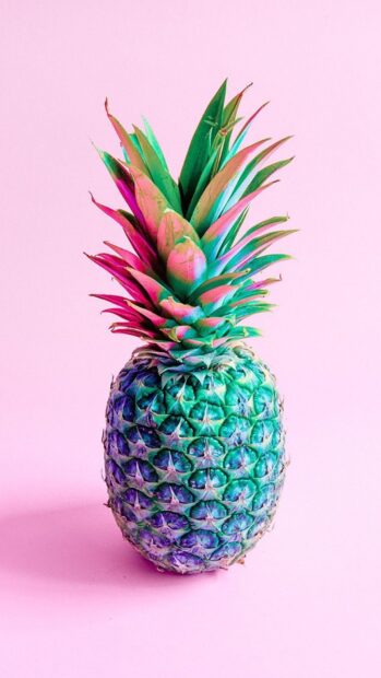 Vibrant pineapple with colorful leaves on a pastel pink background