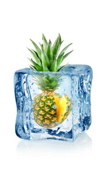 A fresh pineapple frozen inside a clear ice cube with water droplets on a white background