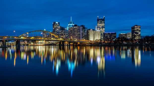 The Pittsburgh city skyline illuminated at night with glowing bridge lights and river reflections