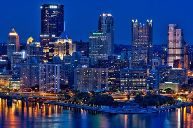 Night view of the Pittsburgh city skyline with illuminated skyscrapers and river reflections