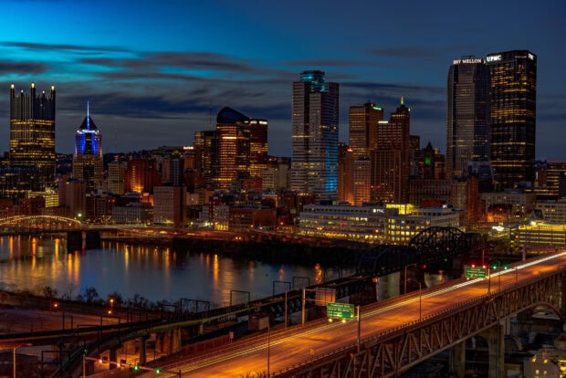 Nighttime cityscape of Pittsburgh skyline with illuminated buildings and bridges