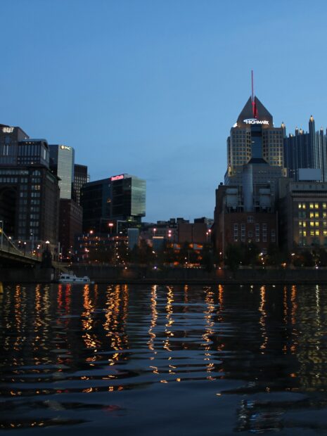 Evening cityscape featuring Pittsburgh skyline reflecting on water at dusk