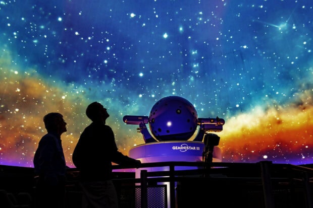 People observing a planetarium projector under a starry display of the cosmos