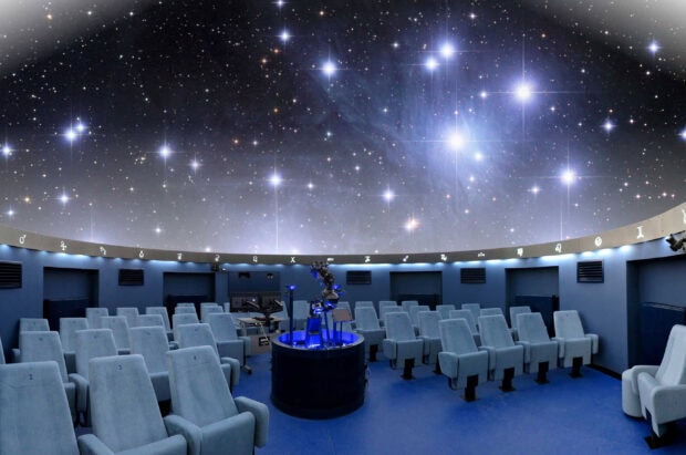 The interior of a planetarium featuring a central projector and a starry sky projection on the dome ceiling