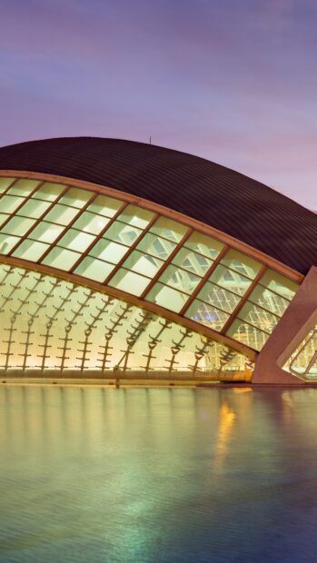 Modern planetarium structure with glass panels reflecting over calm water at dusk
