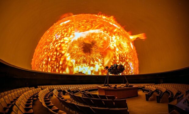 A detailed planetarium projection showing the sun with solar flares in a large dome theater