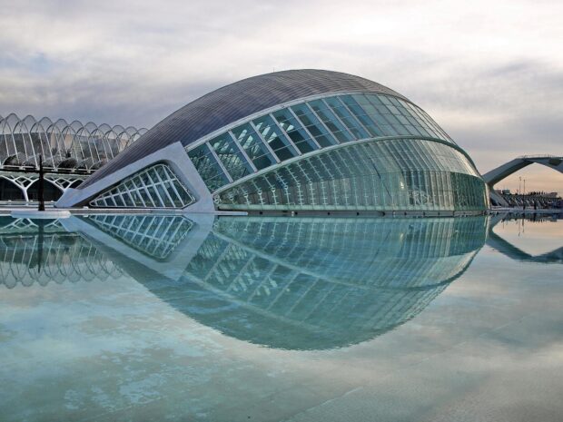 Modern planetarium building reflecting on calm water under cloudy sky