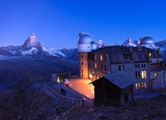 Observatory building with planetarium surrounded by mountains at dusk under a planetarium sky