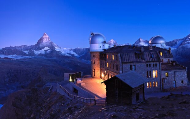 Observatory building with planetarium surrounded by mountains at dusk under a planetarium sky