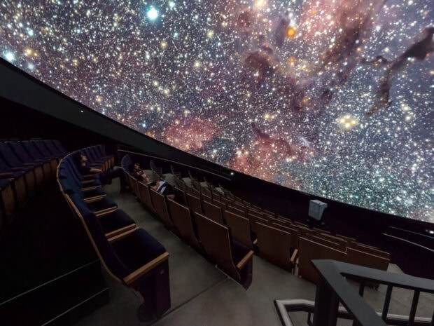 People watching a planetarium projection of a galaxy full of stars and cosmic dust