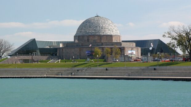A large planetarium building with a domed roof near a waterfront