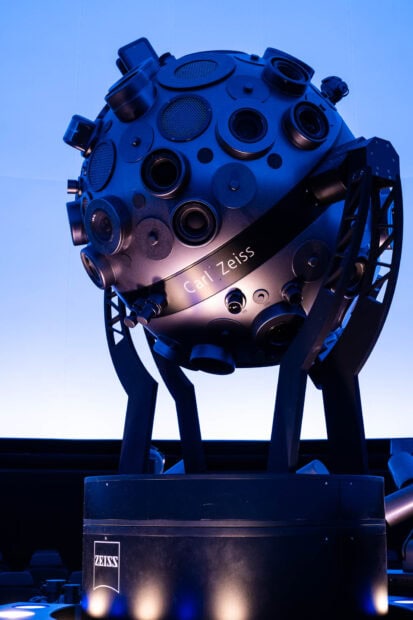 A detailed planetarium device with multiple lenses and the Carl Zeiss logo in a dark room