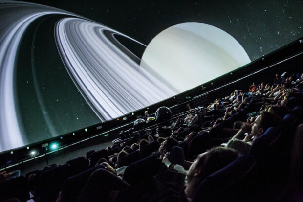 Visitors watching a planetarium projection featuring Saturn's rings in a dark theater