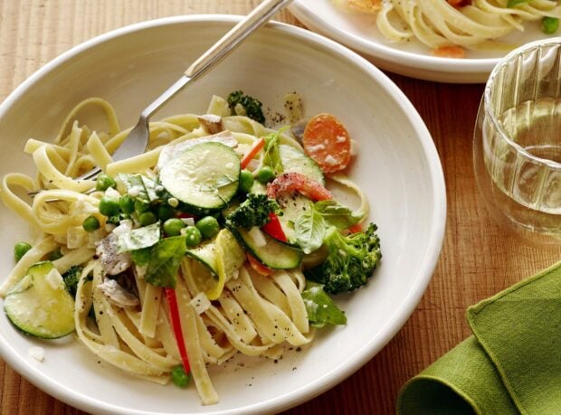 A fresh plate of pasta with vegetables including zucchini peas carrots and broccoli on a white plate