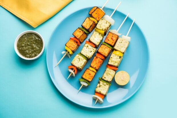 Grilled paneer cubes skewered with vegetables on a plate with green chutney and lemon slice