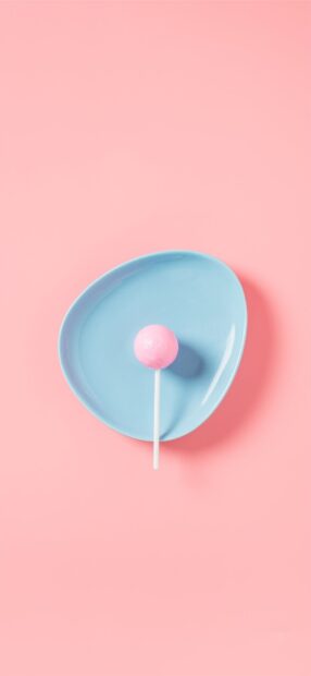 A pink lollipop placed on a blue plate on a pink surface