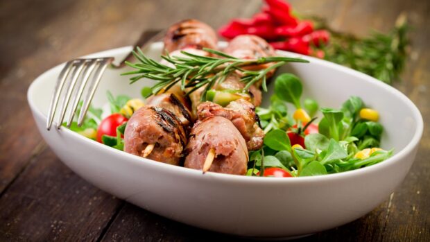 Grilled sausage skewers with fresh vegetable salad and rosemary in a white plate