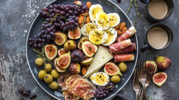 A plate with figs grapes boiled eggs cheese almonds and prosciutto on a rustic table