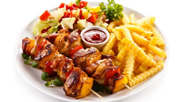 Grilled chicken skewers with vegetables and crinkle cut fries on a white plate